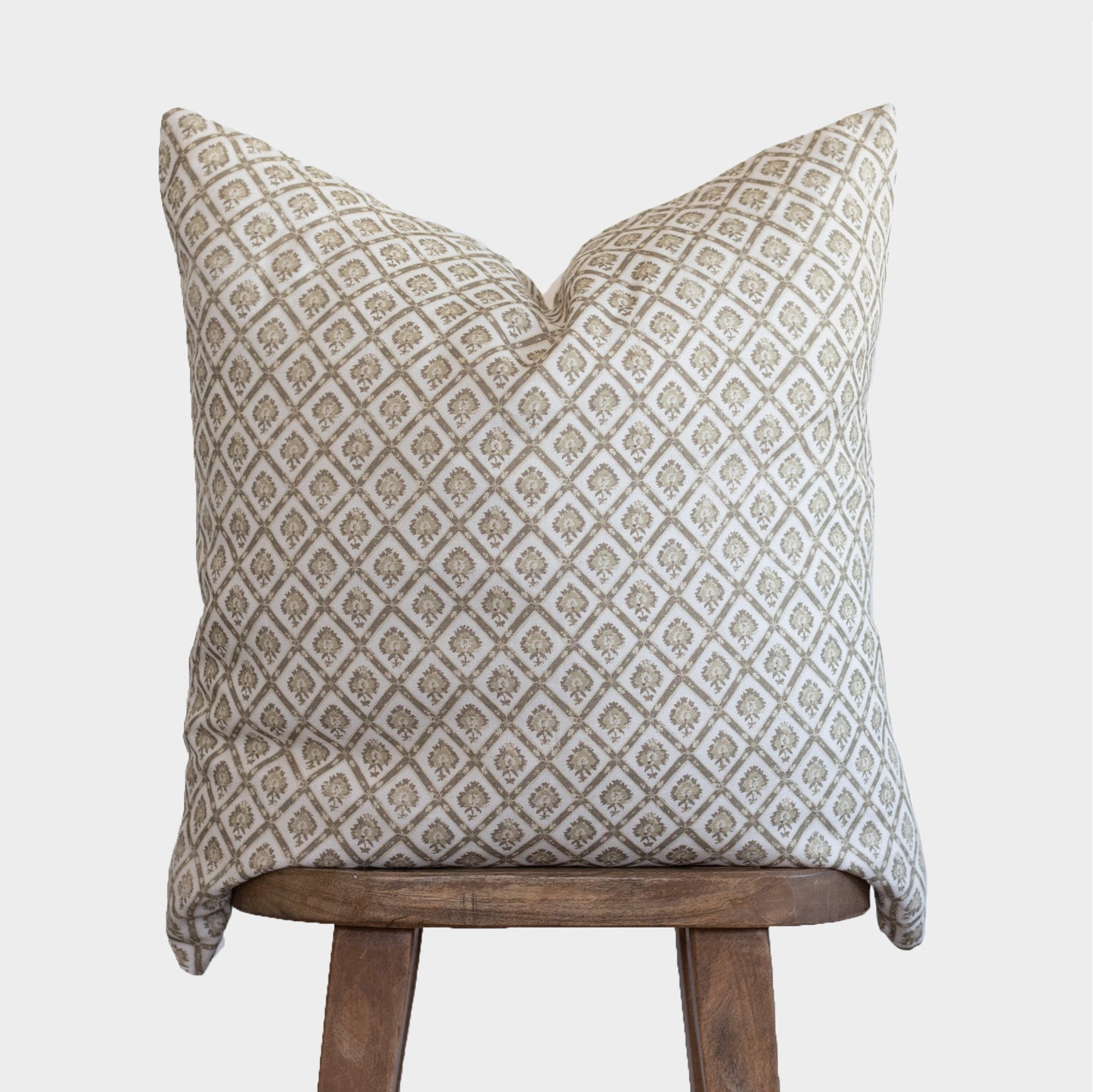 Beige and cream linen pillow with geometric diamond pattern, displayed on wooden stool.