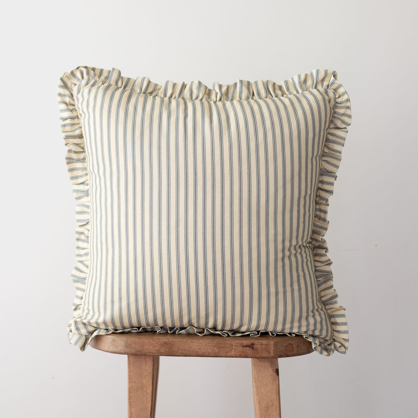 Square throw pillow with vertical stripe pattern and ruffled edges on all sides, displayed on wooden stool.