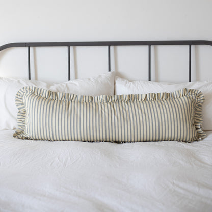 Long rectangular pillow with tan and white vertical stripes and ruffled edges on a bed with white bedding.