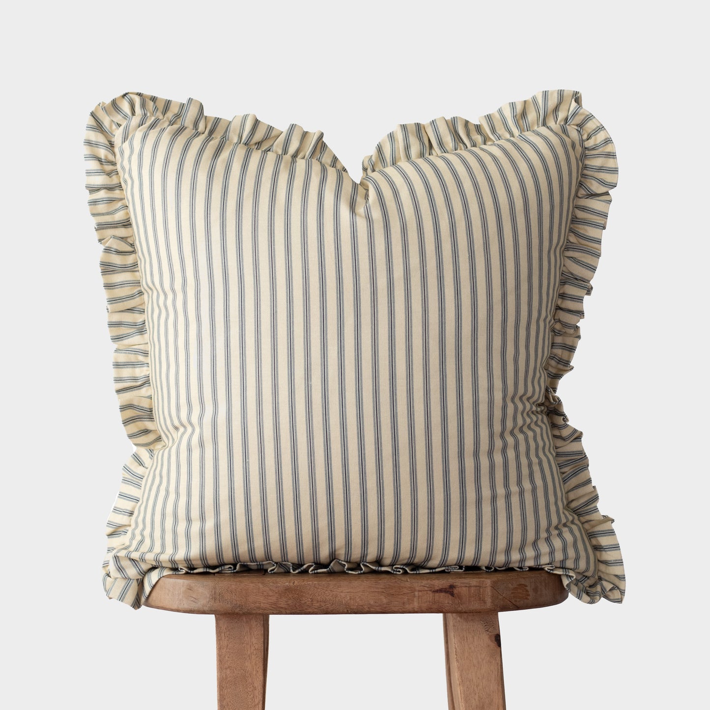 Cream and blue striped pillow with ruffled edges on all sides, displayed on a wooden stand.