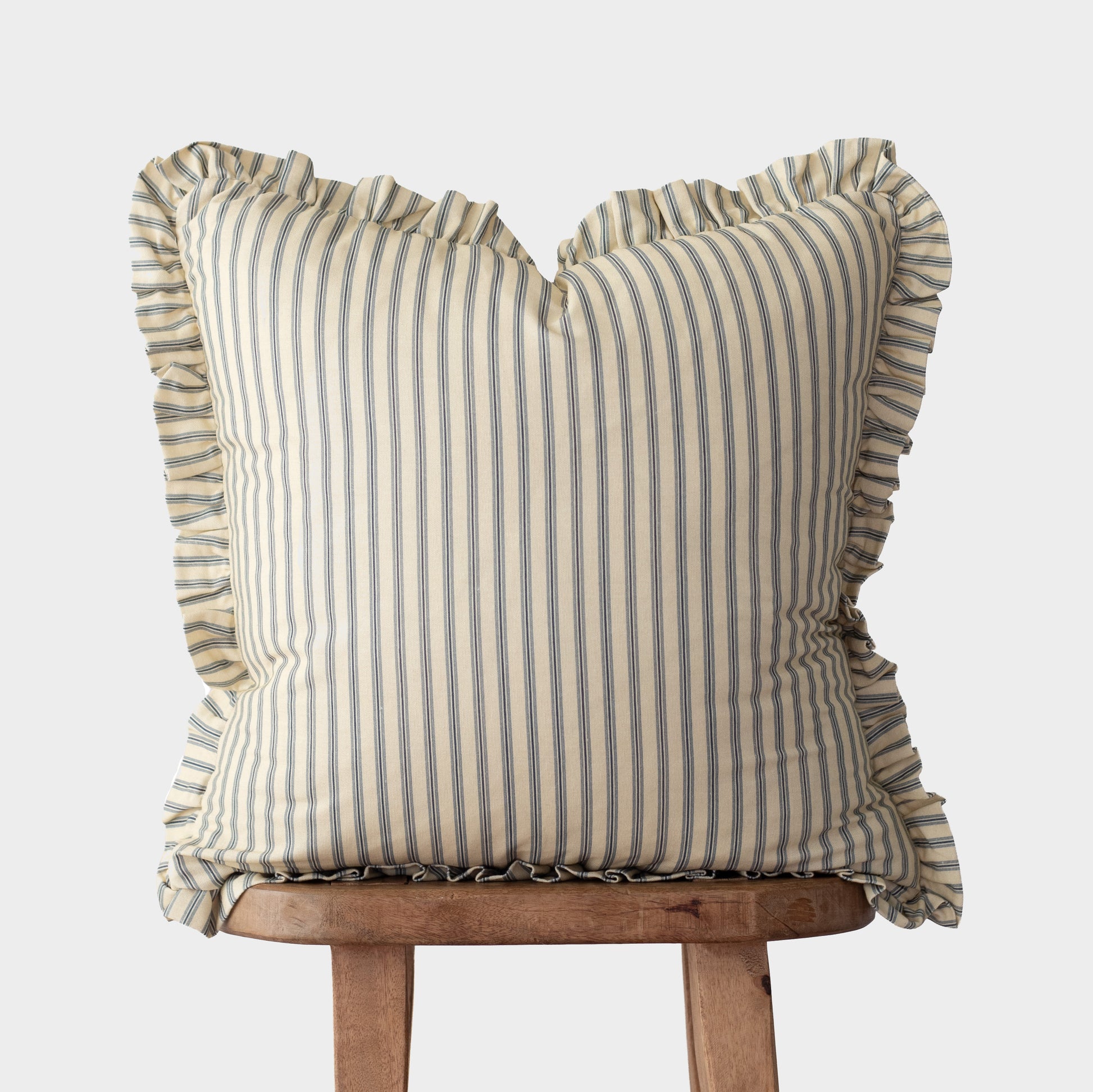 Cream and blue striped pillow with ruffled edges on all sides, displayed on a wooden stand.