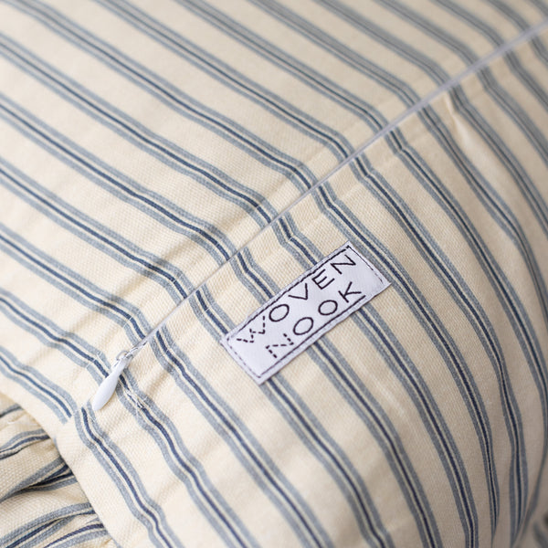 Blue and white striped pillow with ruffled edge and brand label visible.