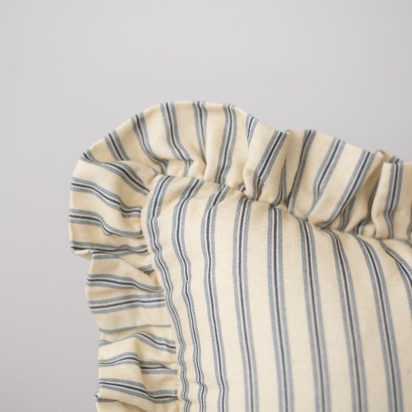 Cream and blue striped pillow with gathered ruffle edge detail along one side.