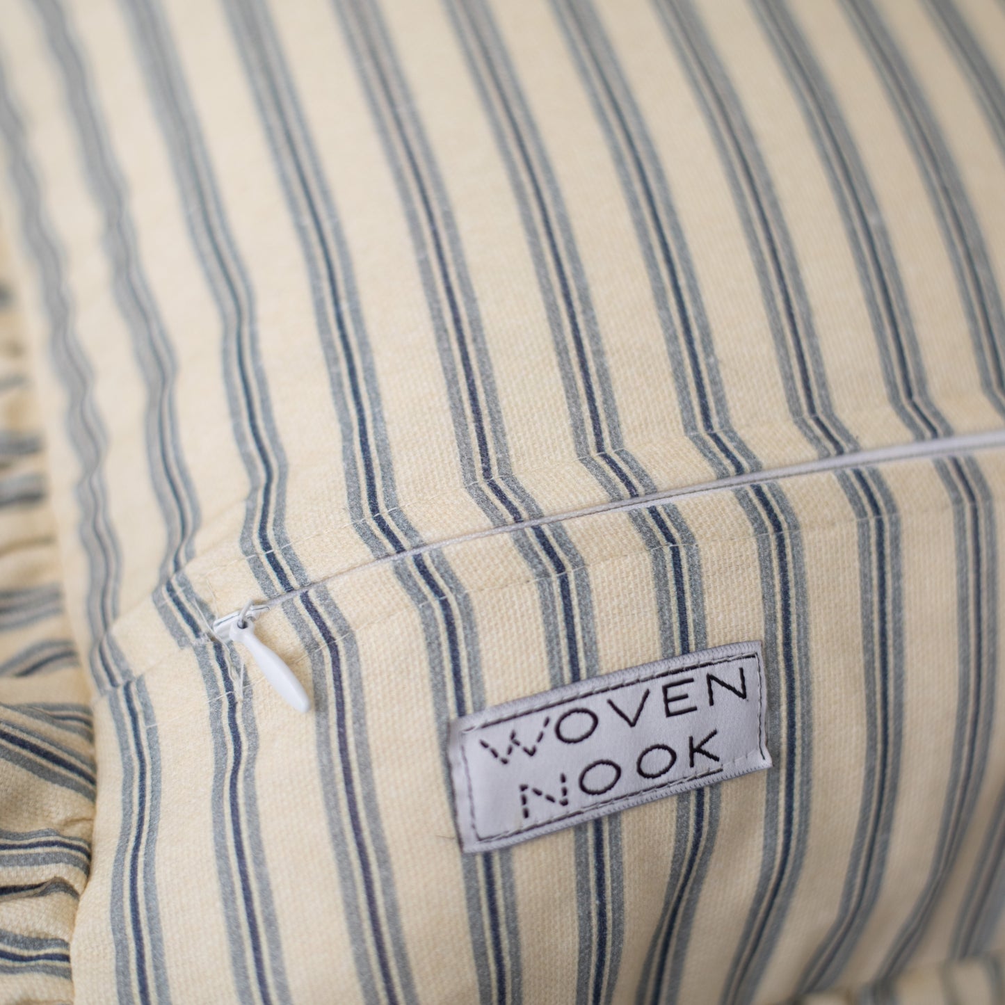 Cream and blue striped pillow with ruffled edge and Woven Nook brand label.