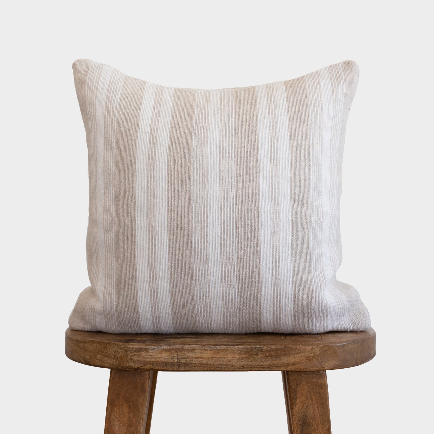 Tan and white striped pillow with vertical texture displayed on wooden chair seat.