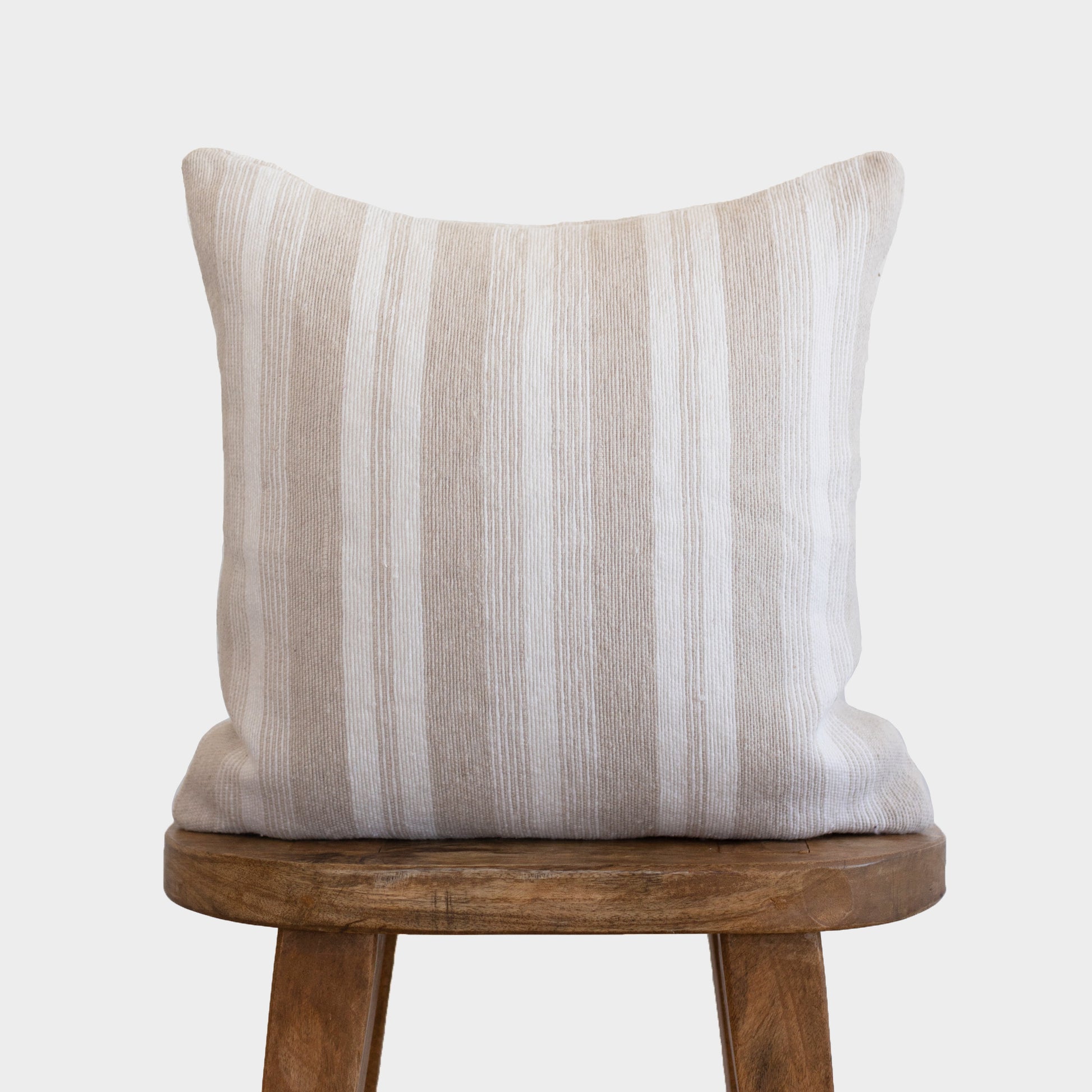 Tan and white striped pillow with vertical texture displayed on wooden chair seat.