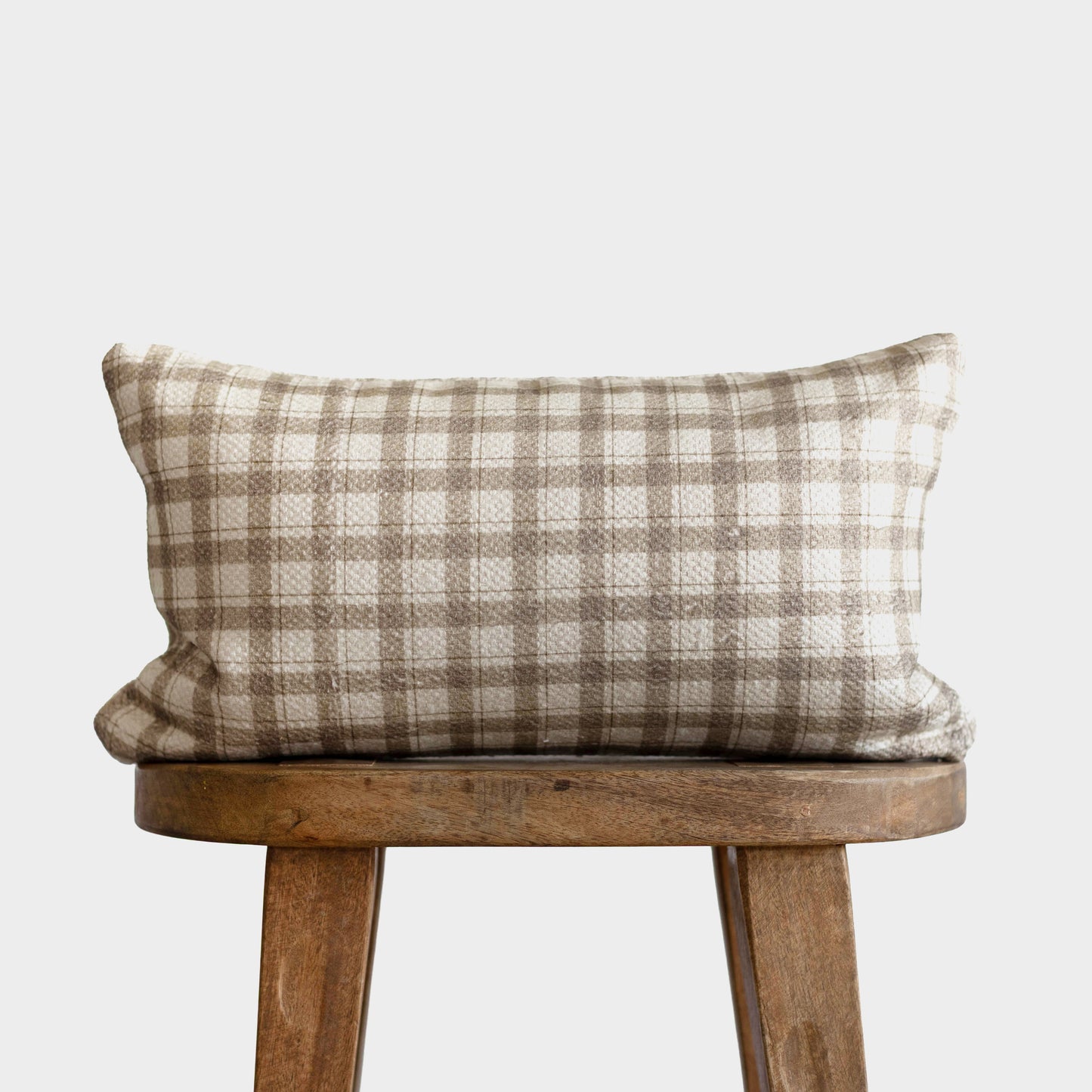 Rectangular lumbar pillow with beige and taupe plaid cotton weave, displayed on wooden stool.