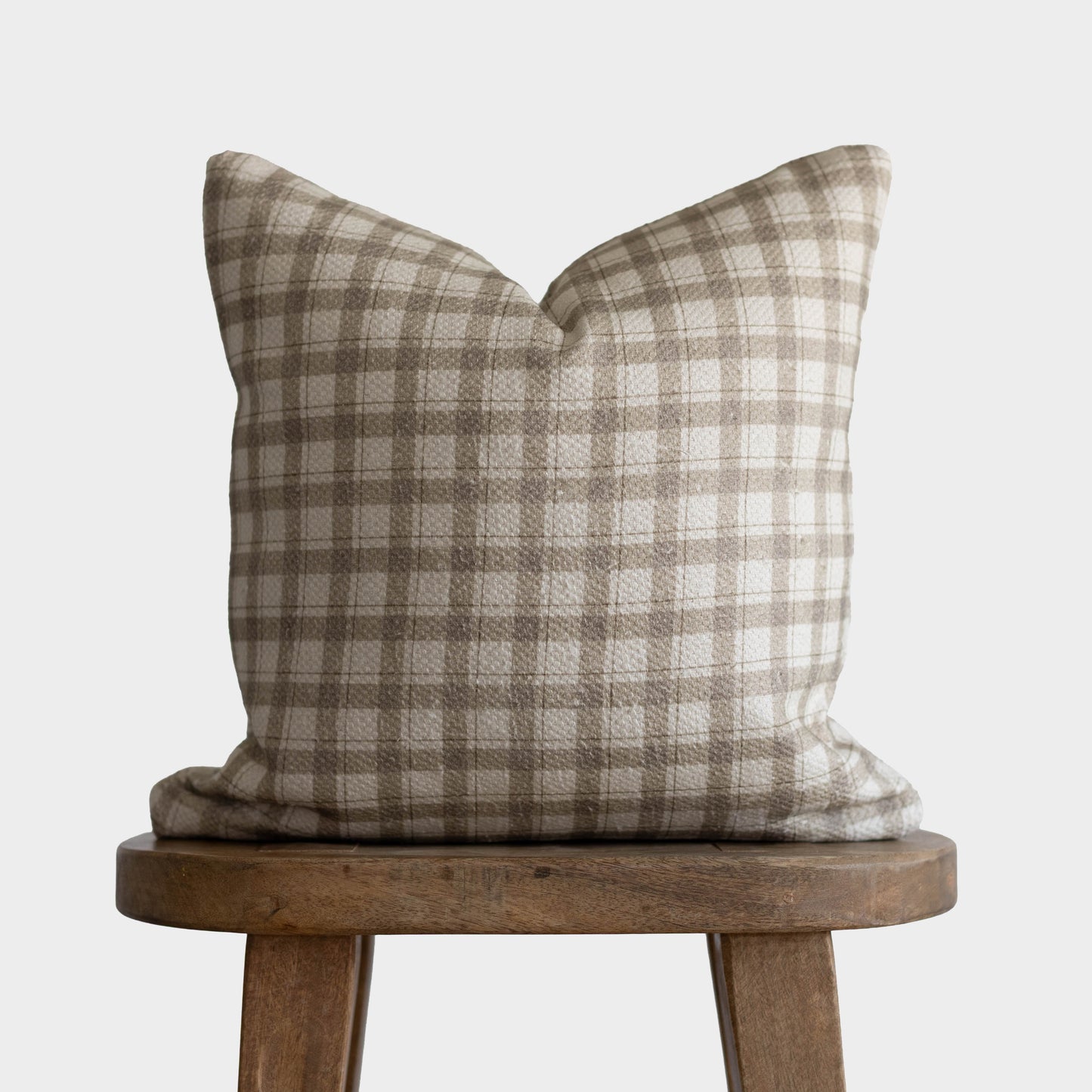 Beige and cream plaid cotton pillow with thick weave texture displayed on wooden stool.