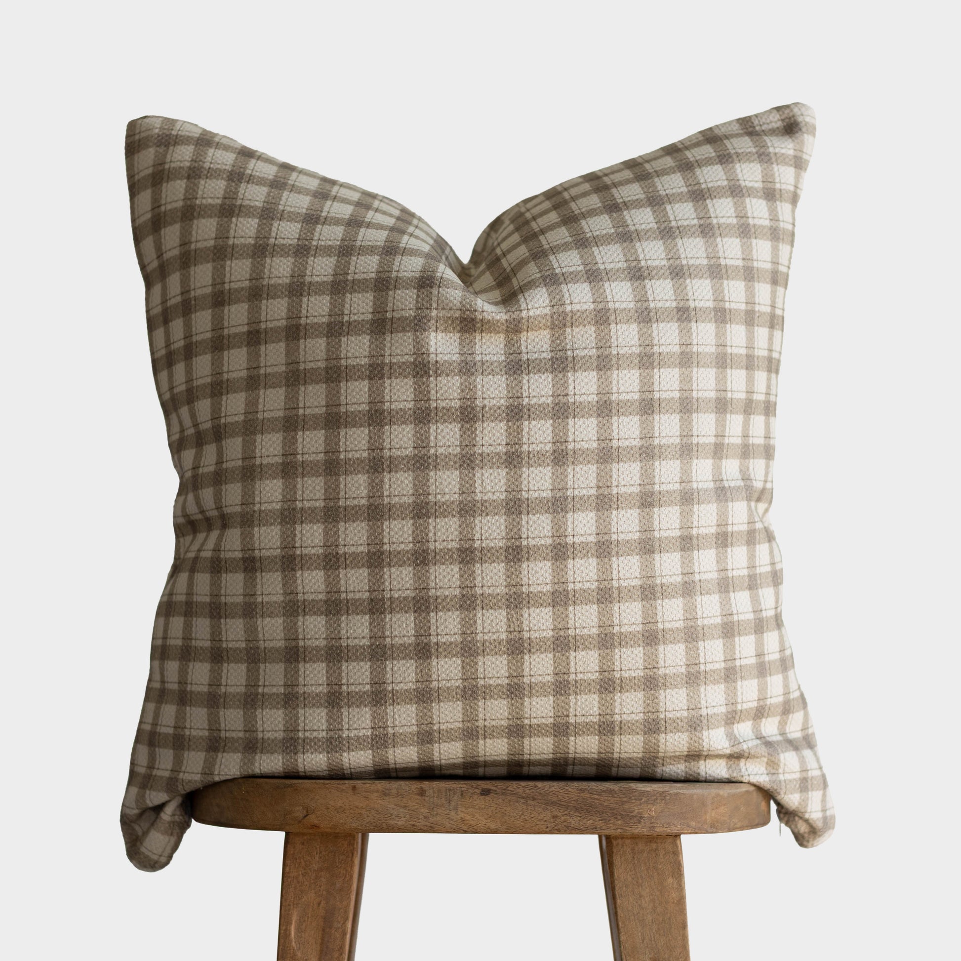 Tan and cream gingham patterned cotton pillow cover with thick weave displayed on wooden stool.