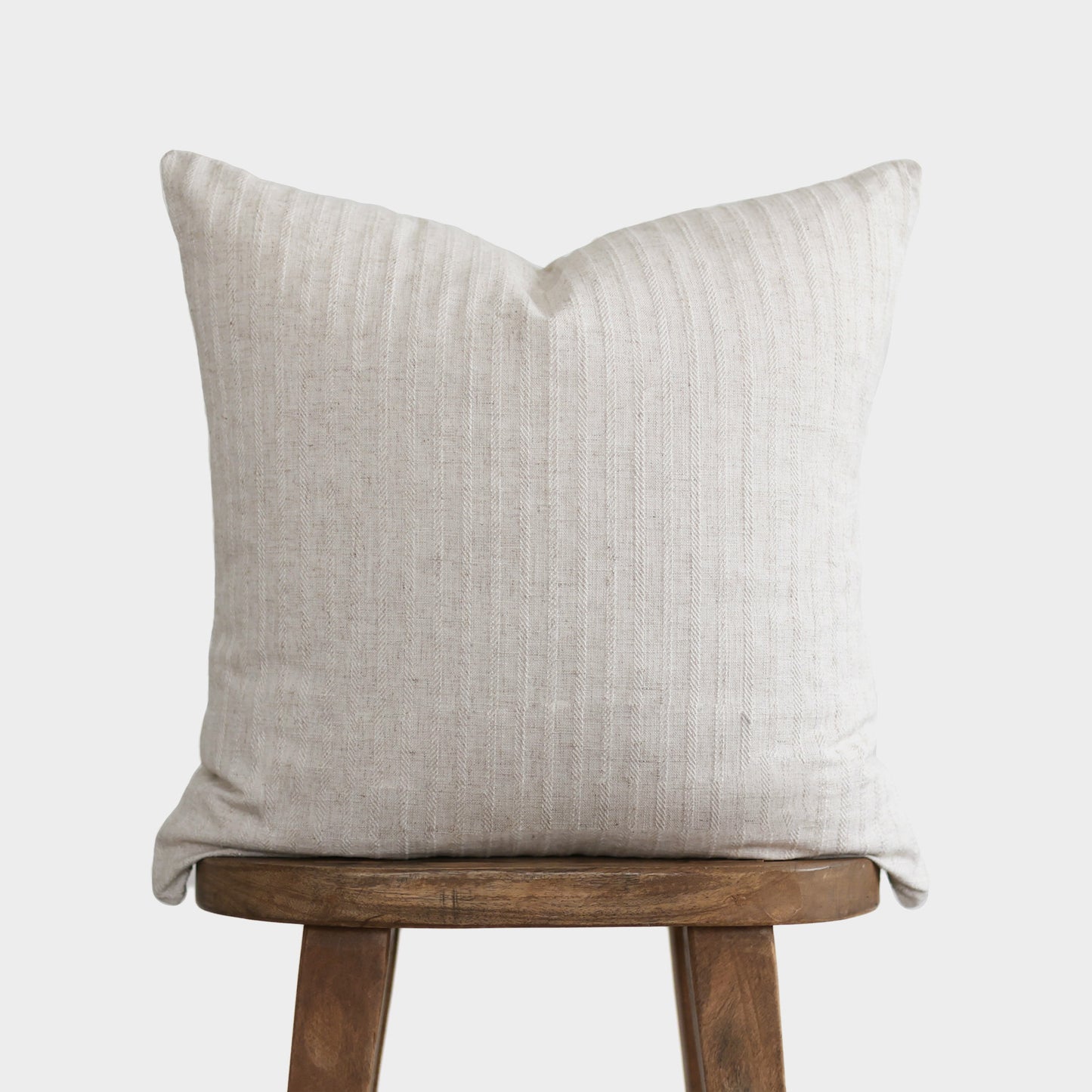 Cream textured pillow with vertical ribbed pattern resting on wooden stool.
