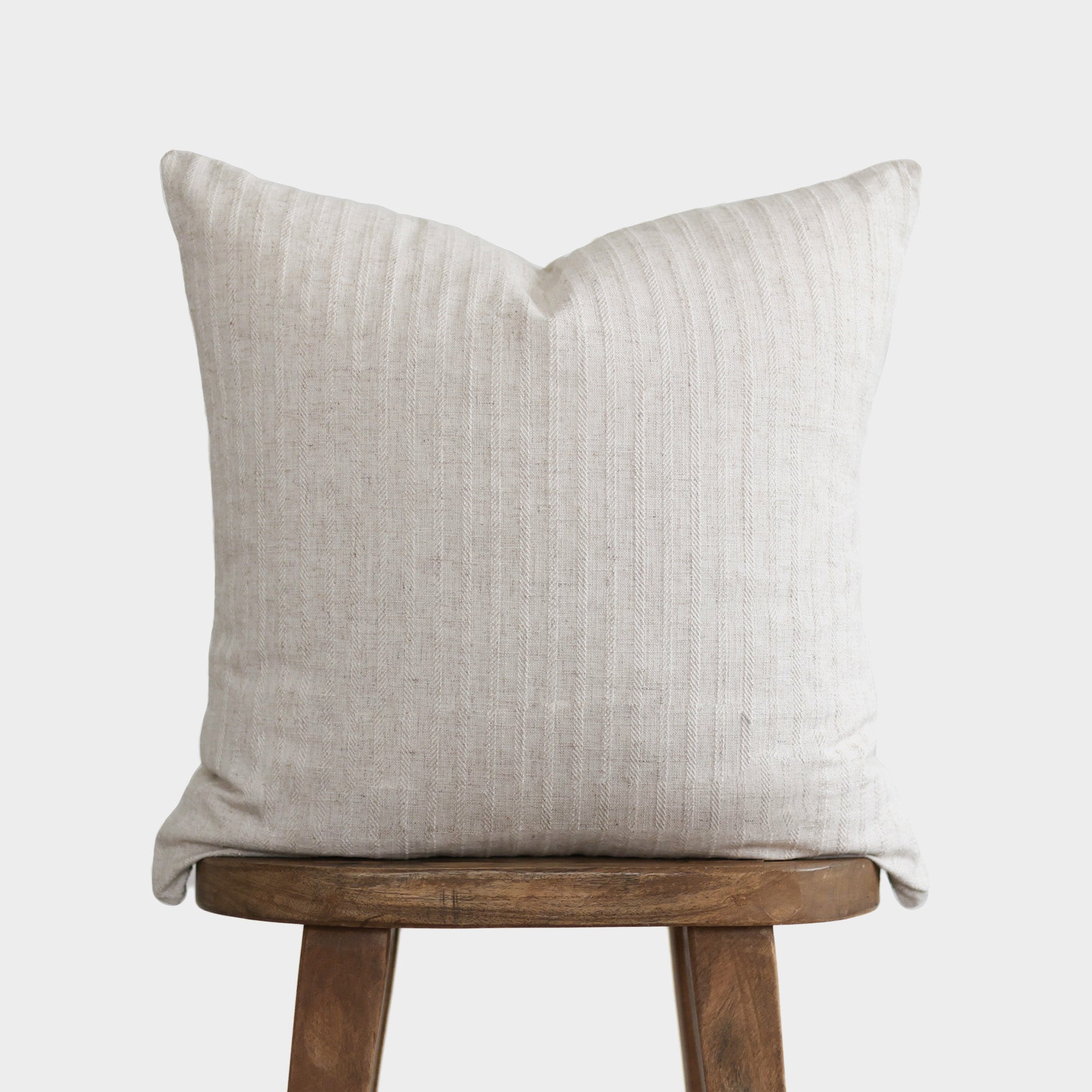 Cream textured pillow with vertical ribbed pattern resting on wooden stool.