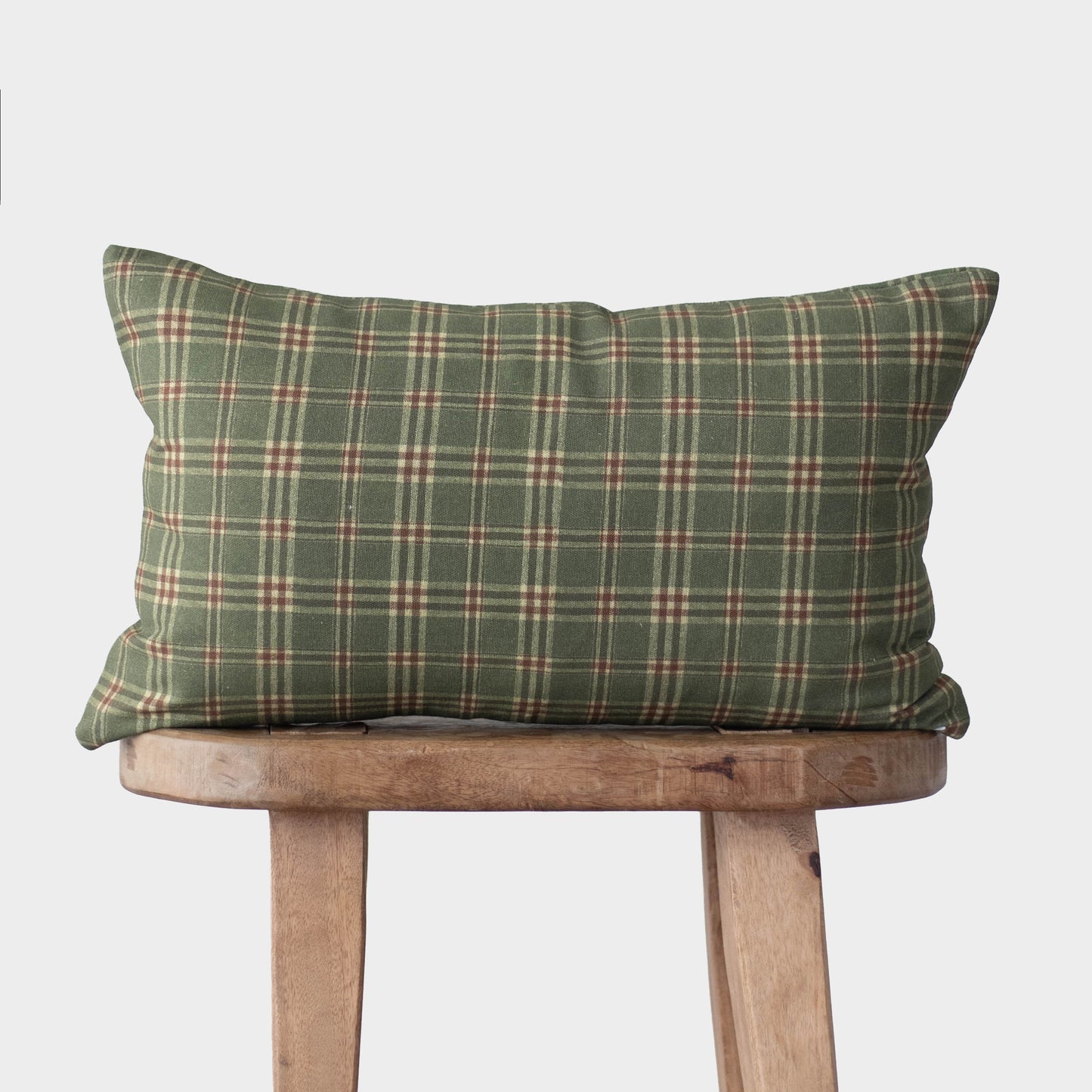 Green plaid pillow with cream and red stripes displayed on a wooden stool.