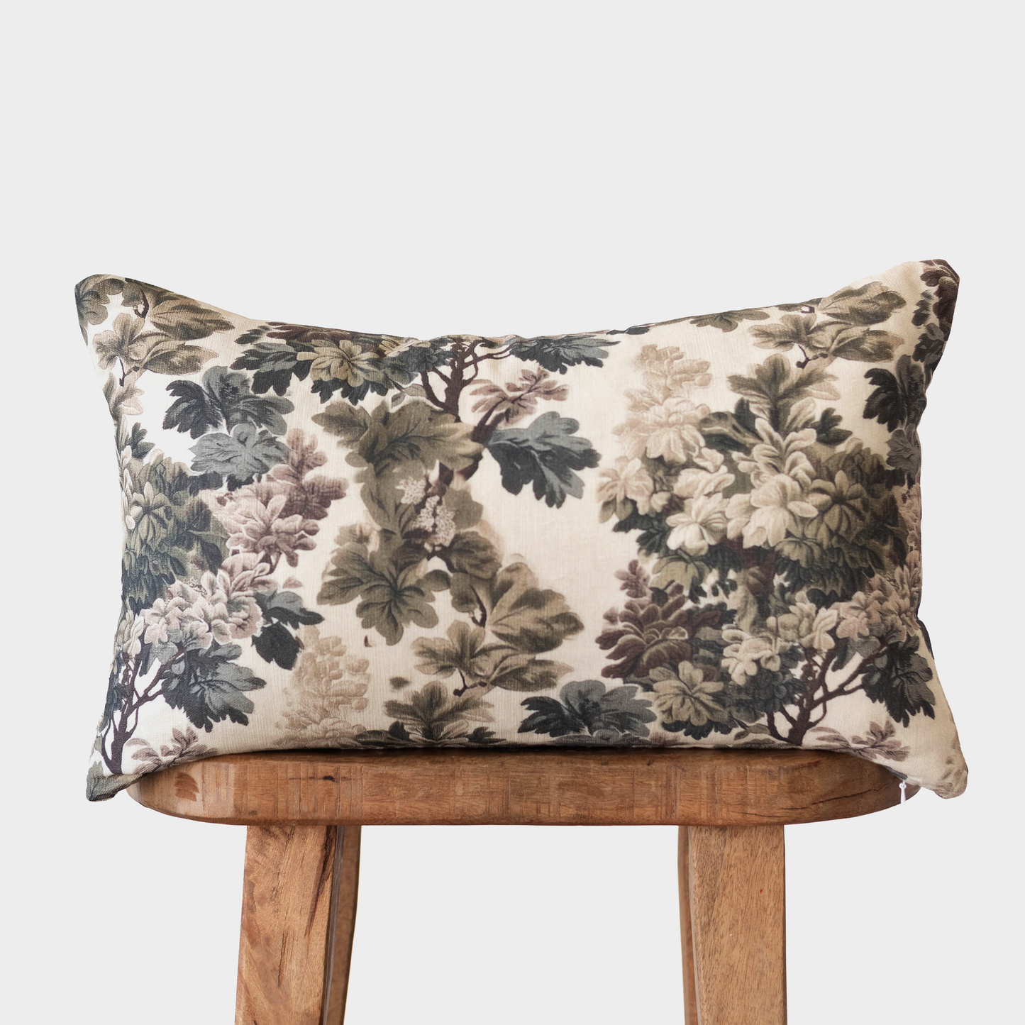 Rectangular pillow with cream background and dark green, taupe, and mauve floral pattern, displayed on wooden chair.
