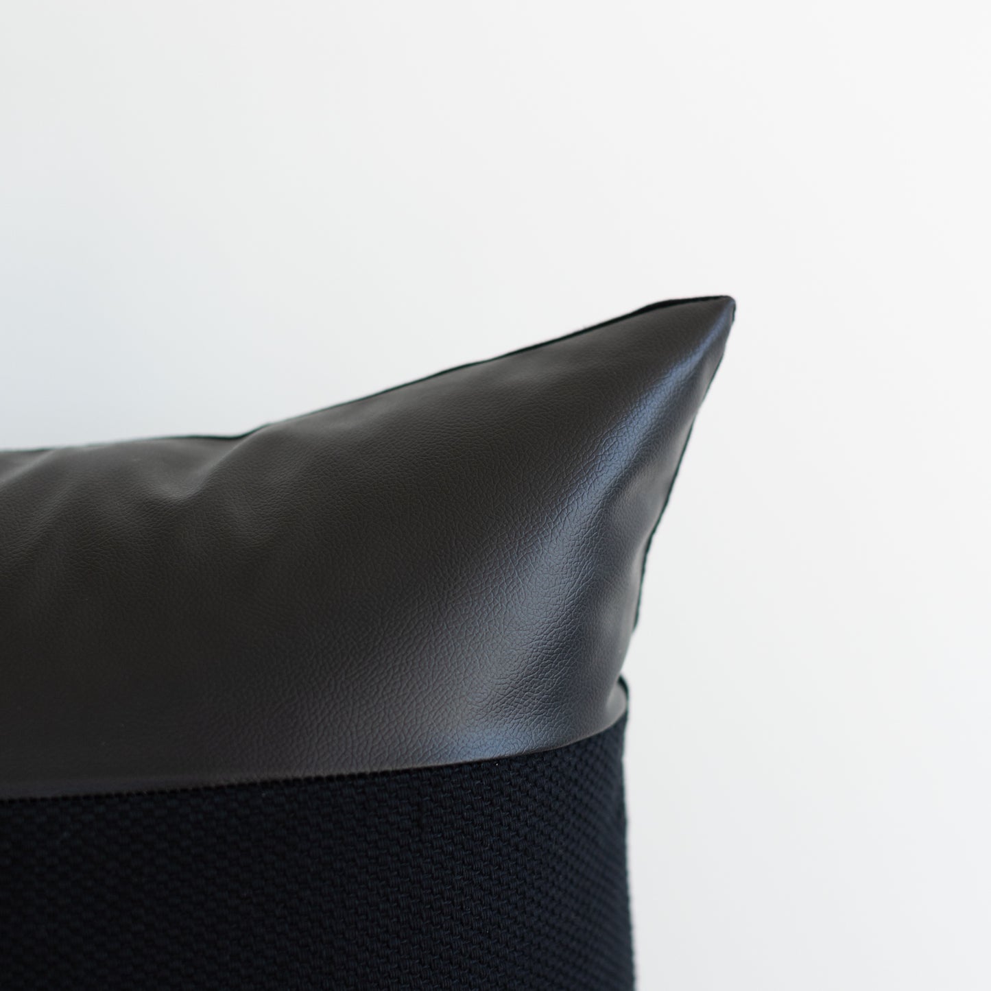 Black pillow with leather top section and textured fabric bottom section.