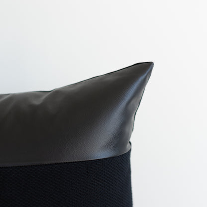 Black pillow with leather top section and textured fabric bottom section.
