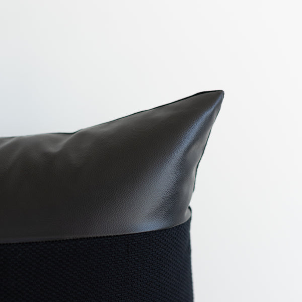 Black pillow with leather top section and textured fabric bottom section.