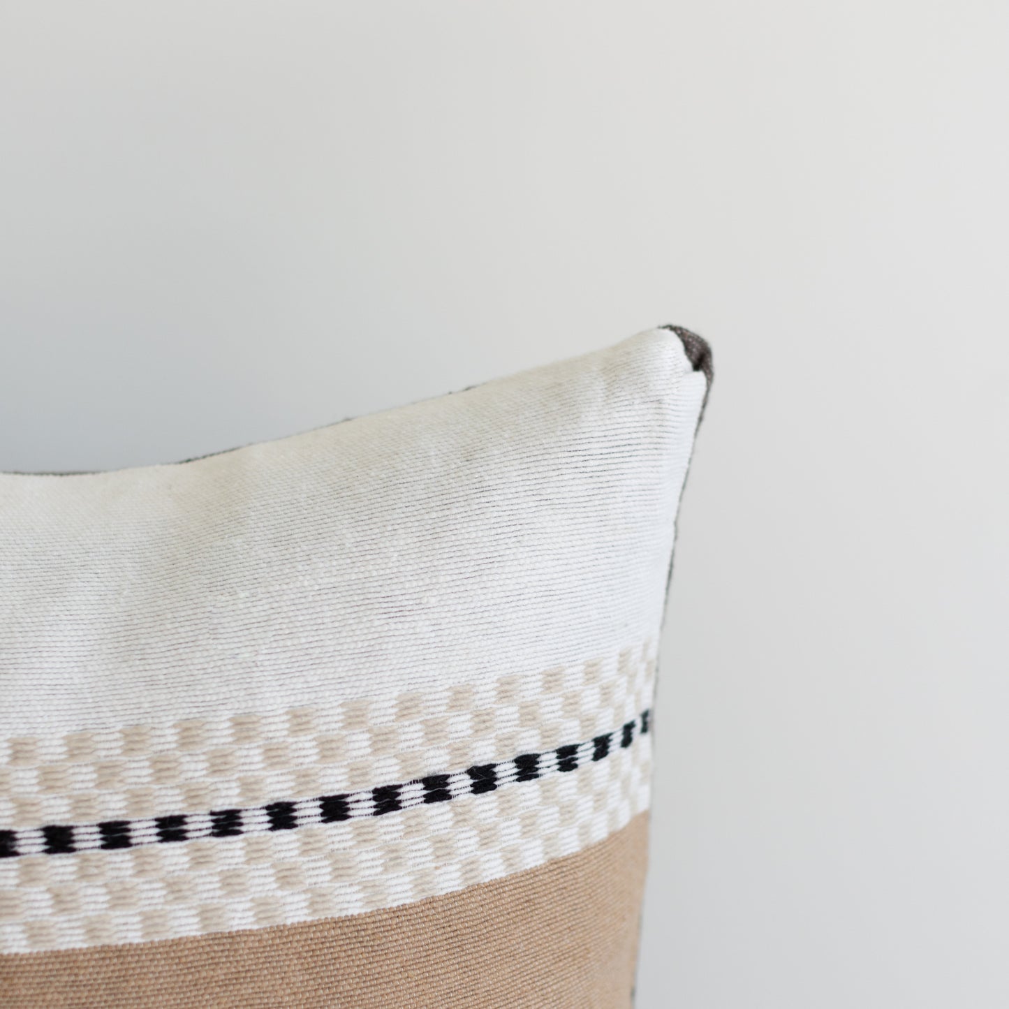 Cream and tan pillow with black stripe trim and folded corner detail.