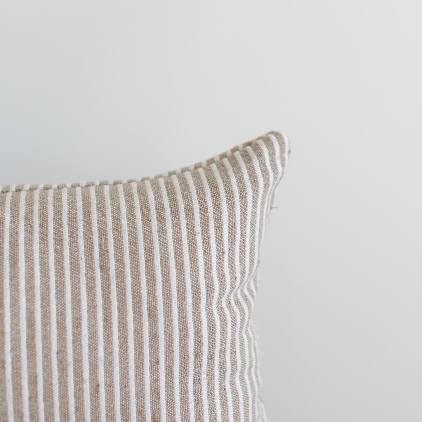Tan and white striped lumbar pillow with vertical ribbed texture and white piping along the edge.