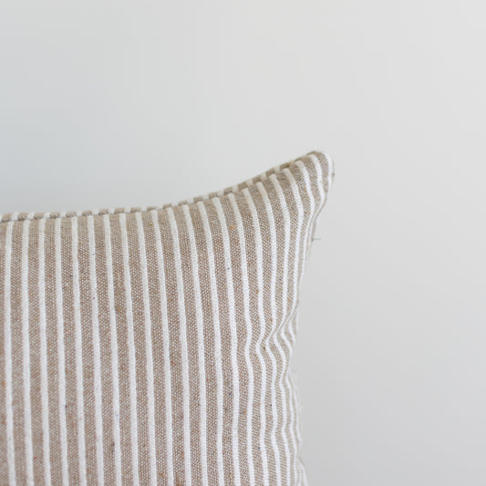 Tan and white striped lumbar pillow with vertical ribbed texture and white piping along the edge.