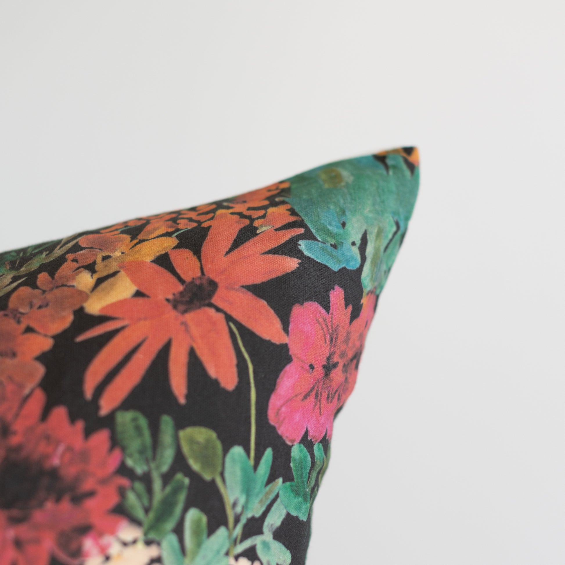 Decorative pillow with dark background and multicolored floral pattern featuring red, pink, orange, and green flowers with gr