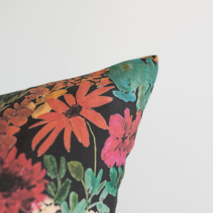 Decorative pillow with dark background and multicolored floral pattern featuring red, pink, orange, and green flowers with gr