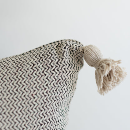 Cream and black tweed pillow with chevron weave pattern and cream tassel corner detail.