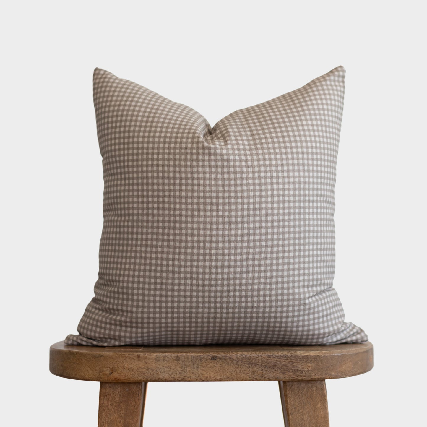 Tan and white gingham patterned pillow with small checks resting on wooden stool.
