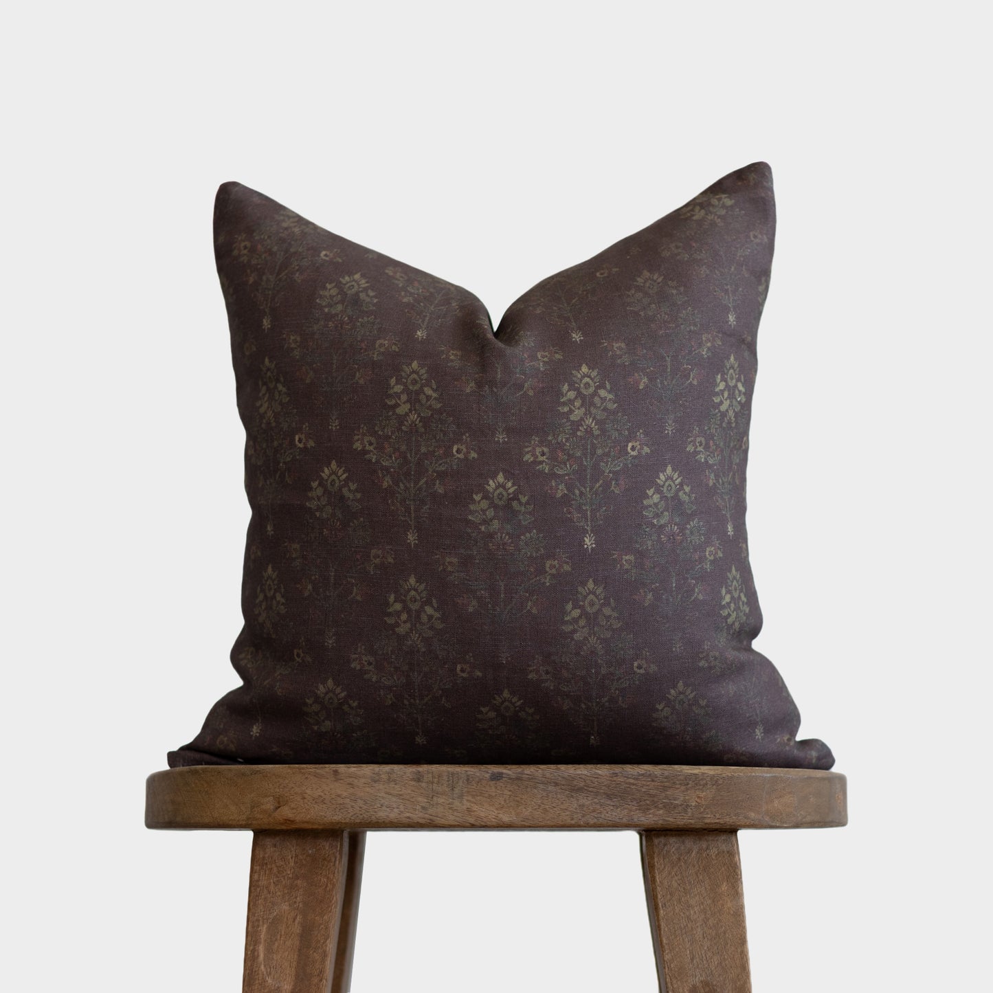 Dark burgundy linen pillow with subtle damask pattern, displayed on wooden stool.