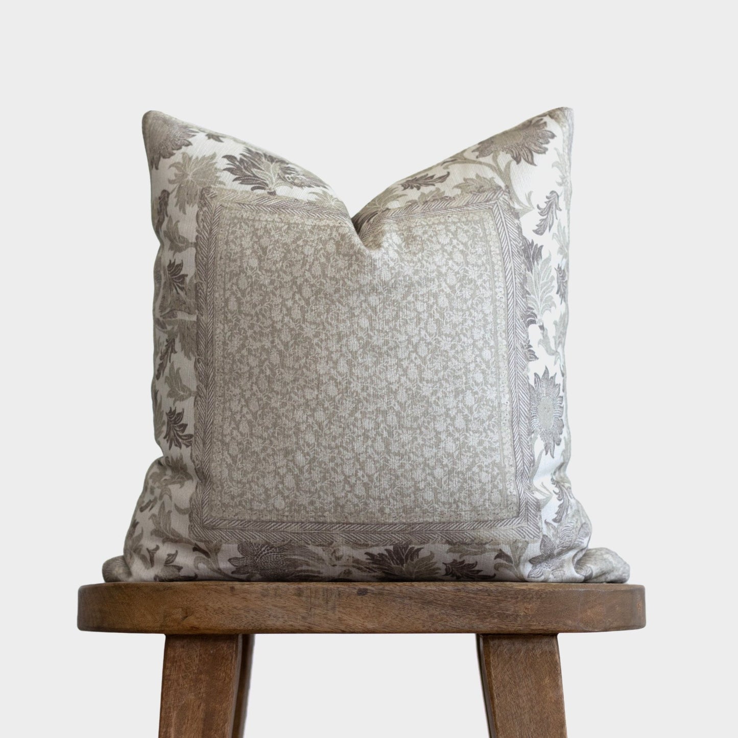 Beige and gray corduroy pillow with botanical leaf pattern border, displayed on wooden stool.