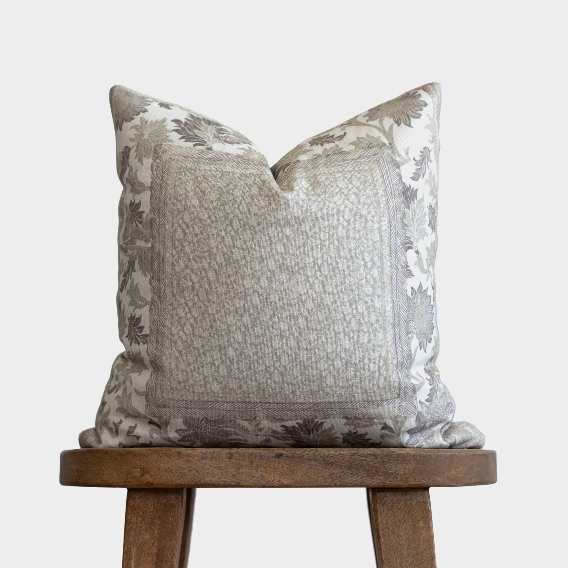 Beige and gray corduroy pillow with botanical leaf pattern border, displayed on wooden stool.