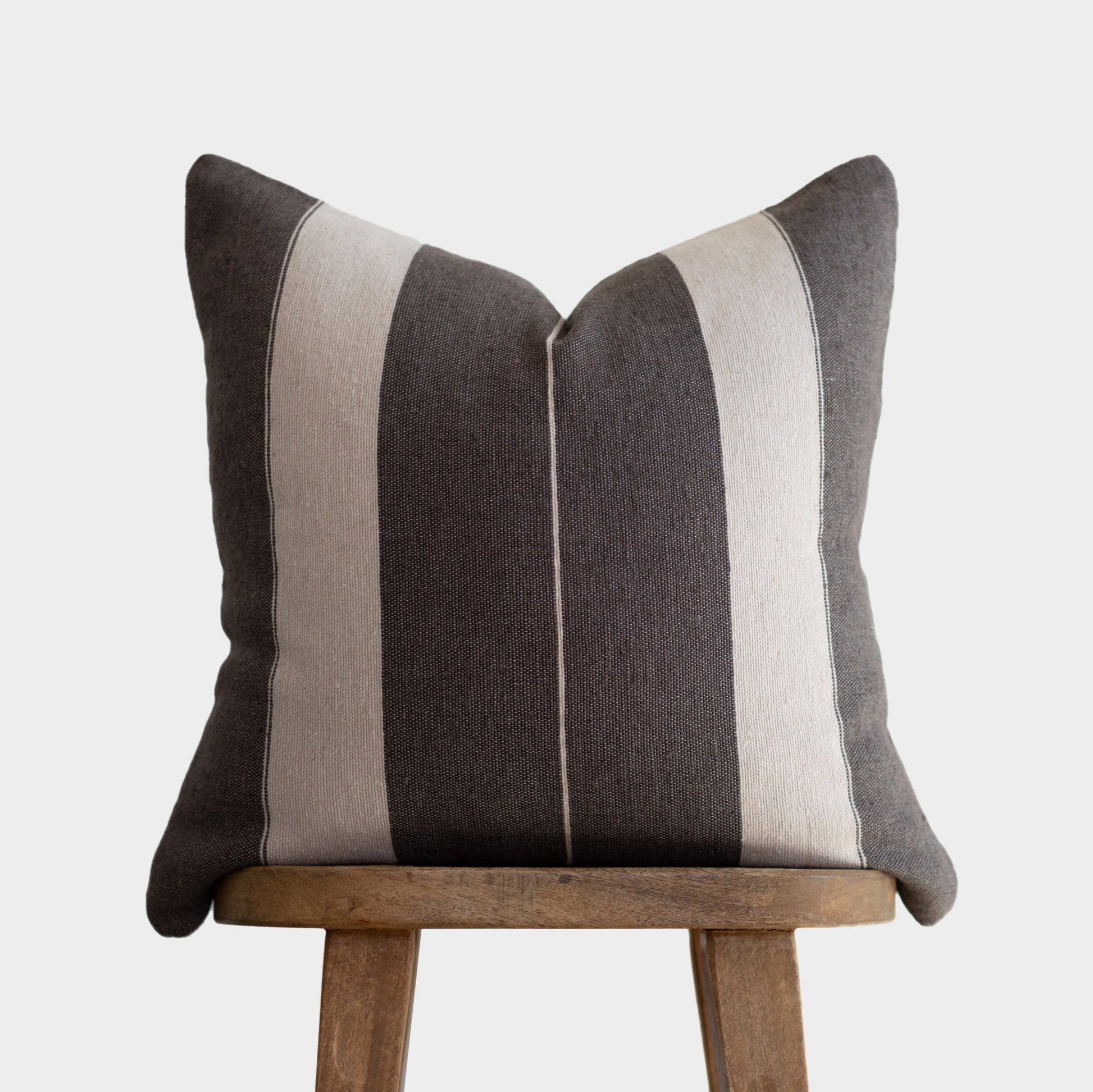 Striped throw pillow in charcoal and cream with vertical bands, displayed on wooden chair.