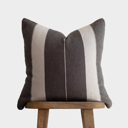 Striped throw pillow in charcoal and cream with vertical bands, displayed on wooden chair.