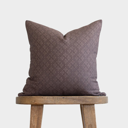 Maroon pillow with quilted diamond pattern displayed on wooden stool.