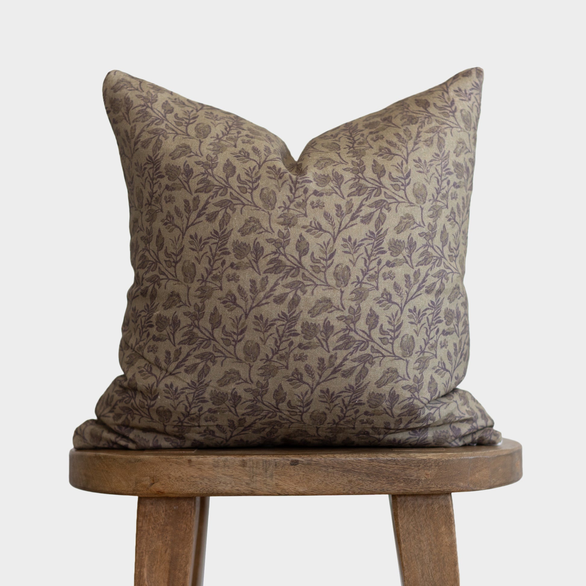 Beige linen pillow with purple floral and botanical print, displayed on wooden stool.