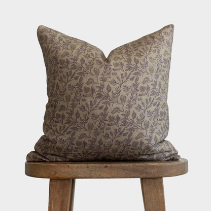 Beige linen pillow with purple floral and botanical print, displayed on wooden stool.