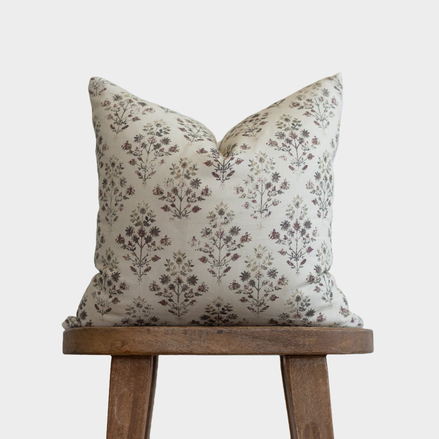 Cream linen pillow with burgundy and green floral botanical print, displayed on wooden stand.