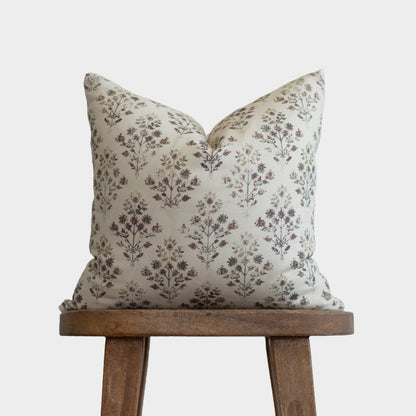 Cream linen pillow with burgundy and green floral botanical print, displayed on wooden stand.