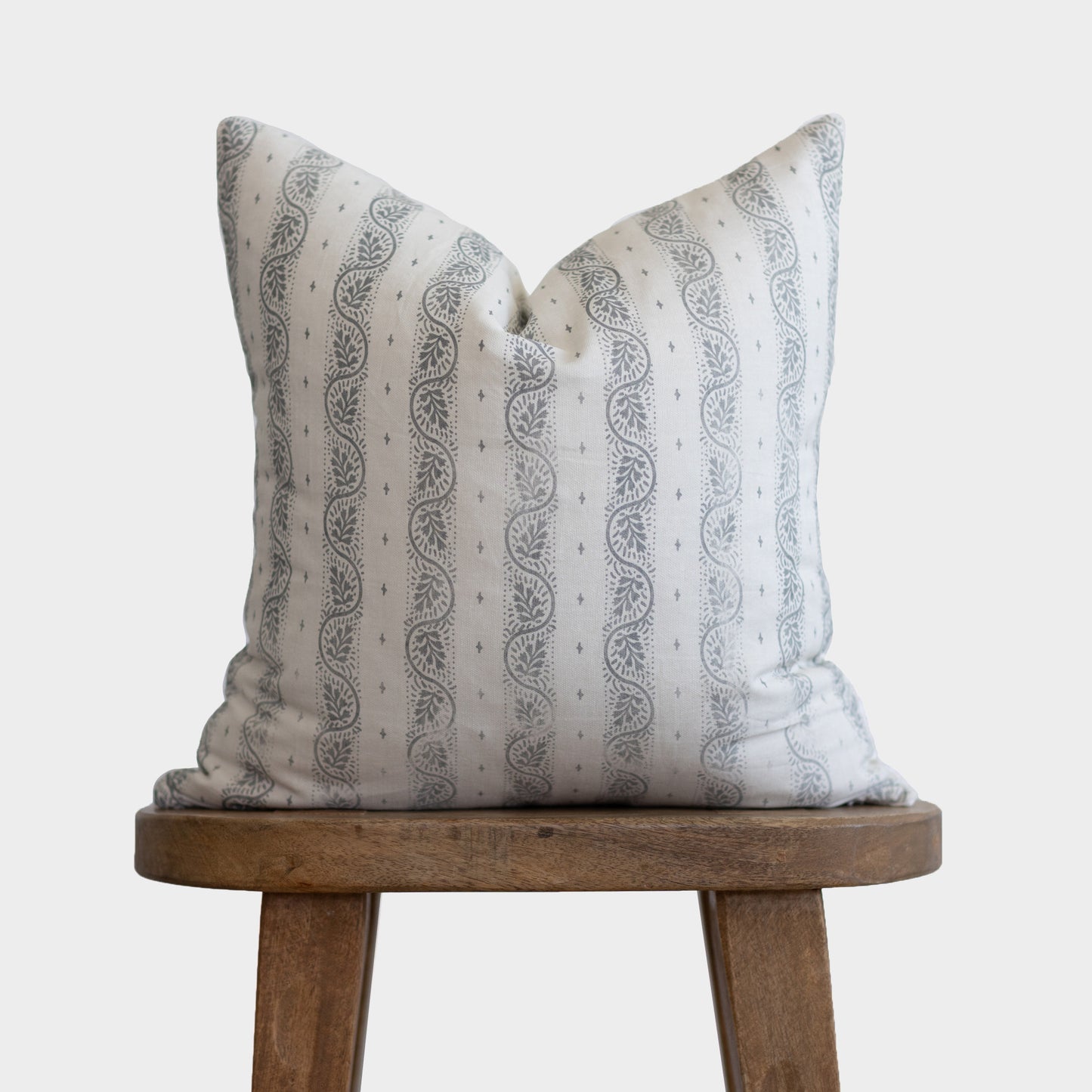 Cream pillow with gray leaf and dot pattern, displayed on wooden stool.