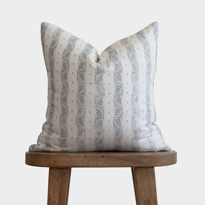 Cream pillow with gray leaf and dot pattern, displayed on wooden stool.