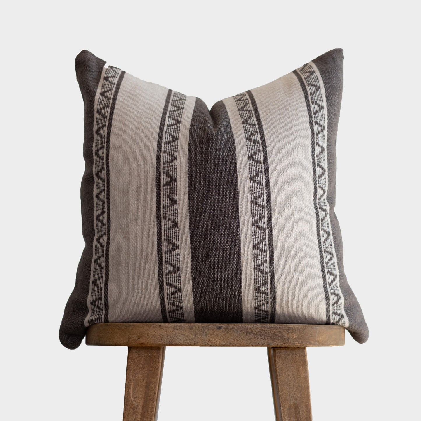 Striped throw pillow in charcoal and cream with geometric pattern trim, displayed on wooden stand.