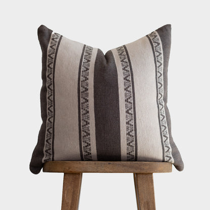 Striped throw pillow in charcoal and cream with geometric pattern trim, displayed on wooden stand.