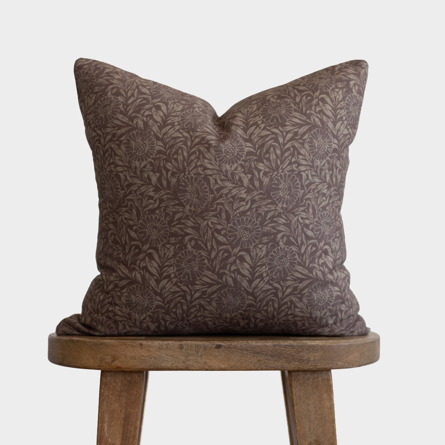 Brown damask patterned pillow with leaf and floral motifs displayed on a wooden stool.