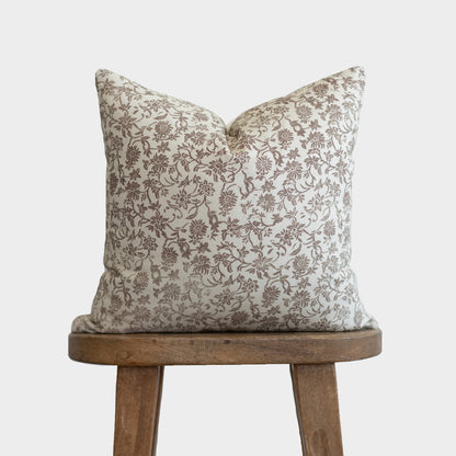 Cream pillow with brown floral and botanical pattern displayed on wooden stool.