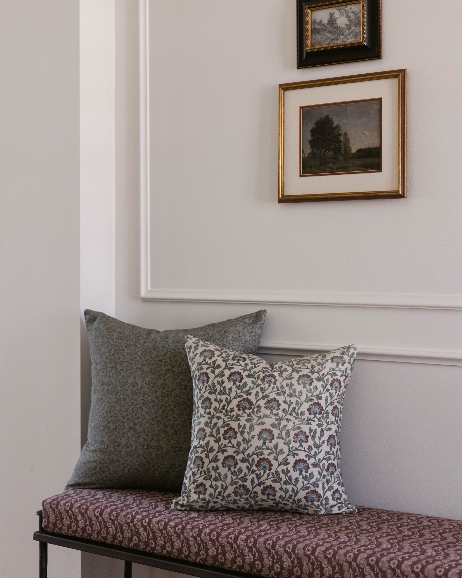 Green wool throw pillow displayed on a bench with patterned cushions against a wall with framed artwork.