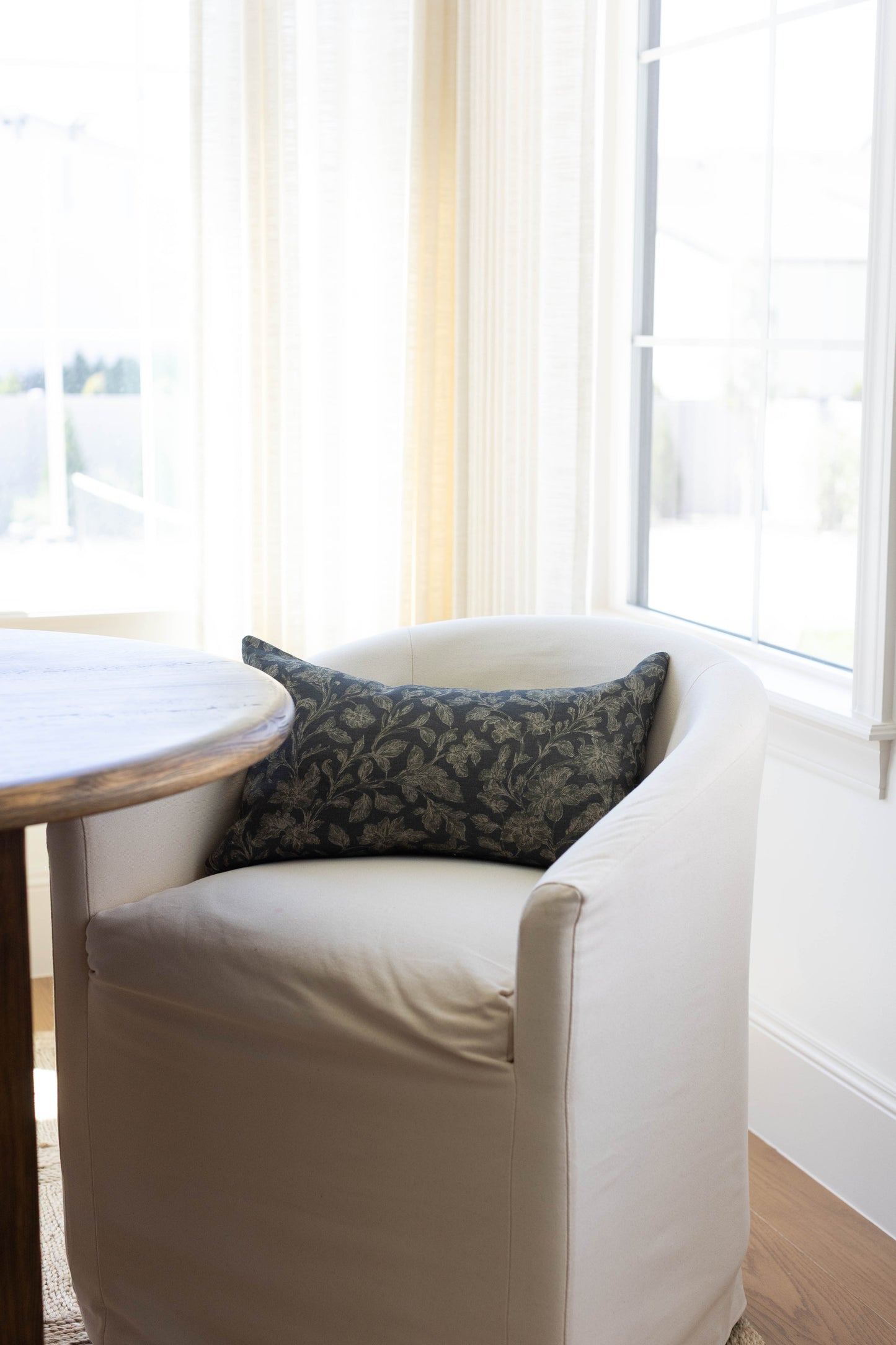 Dark damask patterned pillow with black and gold tones displayed on a cream upholstered chair.