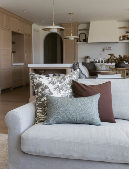 Light gray sofa with decorative pillows in toile, blue, and brown patterns in modern kitchen and living room setting.