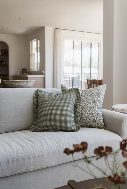 Green and white gingham patterned pillow with ruffled edges on light gray sofa.