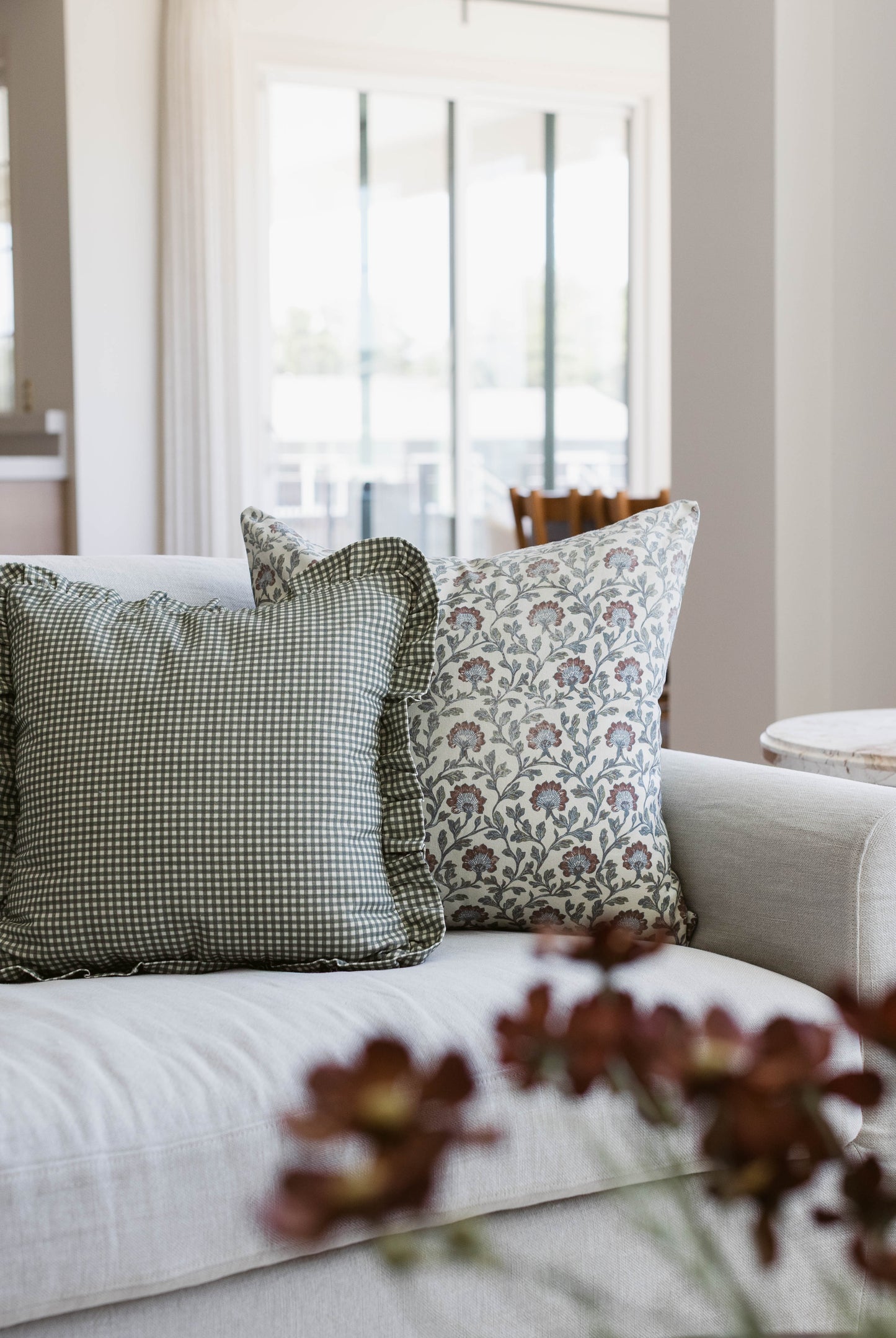 Green and white gingham pillow with ruffle edge on beige sofa.