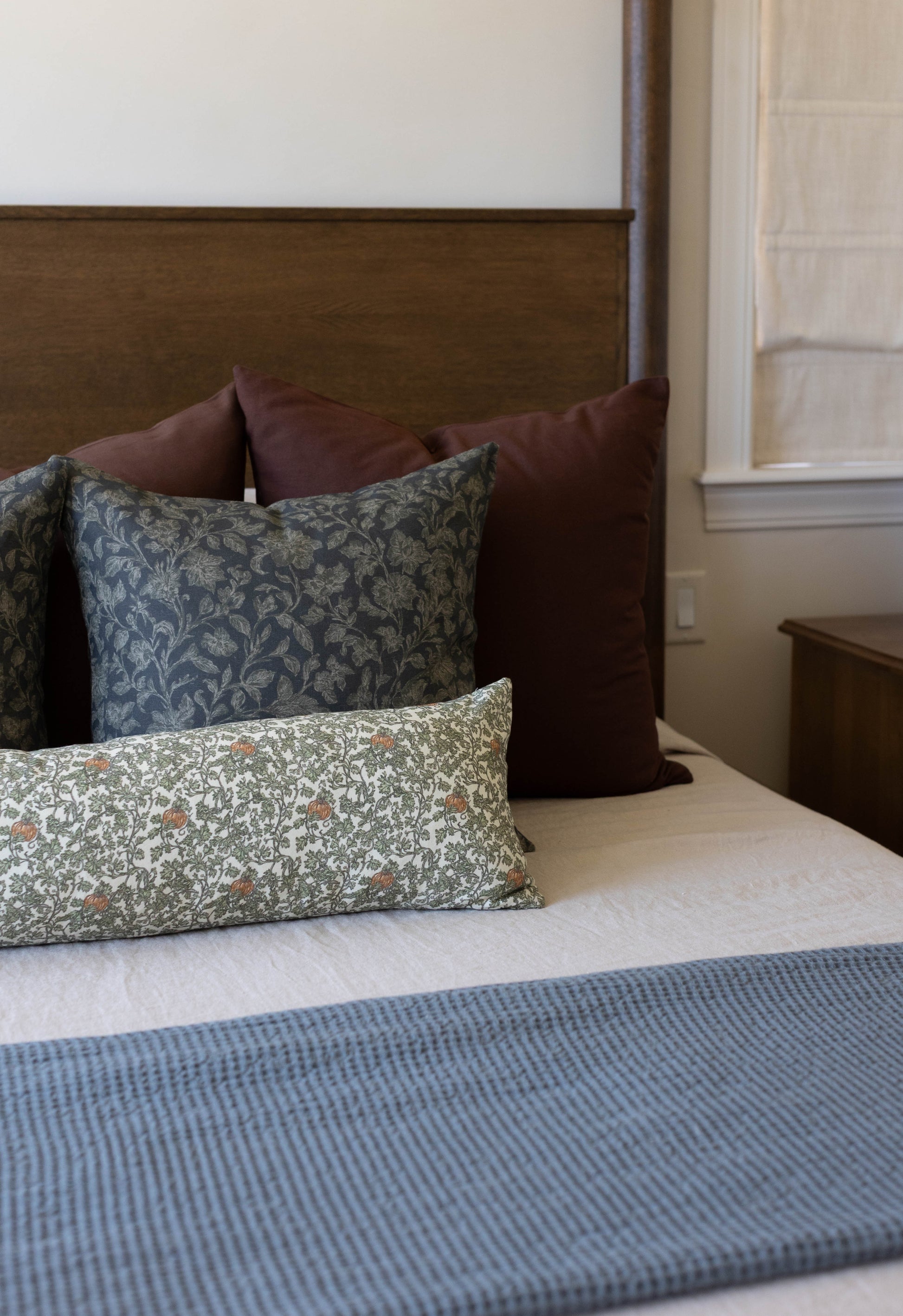 Rectangular pillow with gray-blue floral and botanical pattern displayed on bed with burgundy pillows.