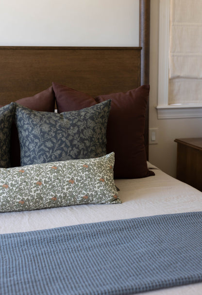 Decorative pillows arranged on a bed with wood headboard, including patterned and solid burgundy pillows.